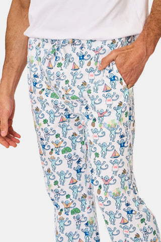 A person is wearing the Mens Charleston Monkey Simon Pant by Roller Rabbit, crafted from soft Pima cotton with a playful monkey print adorned with colorful boats and trees. Their hand rests in the pocket, and only their torso and upper legs are shown.
