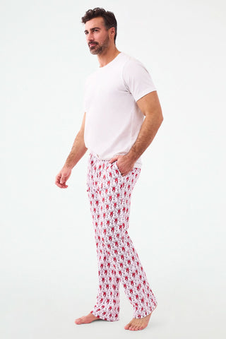 A person stands barefoot, lower half visible, wearing Roller Rabbit's Campus Mens Lovely Monkey Simon Pant—white Pima cotton pants with a red and black monkey pattern and a drawstring waist, one hand in their pocket.