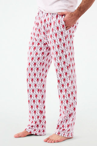 A person stands barefoot, lower half visible, wearing Roller Rabbit's Campus Mens Lovely Monkey Simon Pant—white Pima cotton pants with a red and black monkey pattern and a drawstring waist, one hand in their pocket.