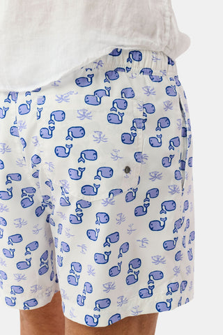A close-up of the Mens Moby Swim Trunk with a blue whale and coral design on white quick-dry fabric. The image highlights the mesh-lined back pocket, waistband, and a tucked-in white shirt.