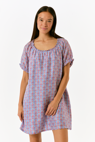 A person wearing the SAPPHIRE Mia Floral Briella Dress, a short-sleeved, blue floral babydoll mini dress with a gathered, rounded neckline and puff sleeves.