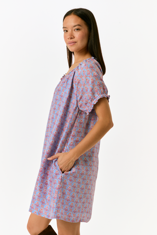 A person wearing the SAPPHIRE Mia Floral Briella Dress, a short-sleeved, blue floral babydoll mini dress with a gathered, rounded neckline and puff sleeves.