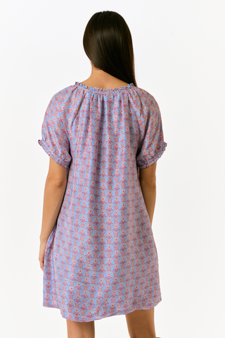 A person wearing the SAPPHIRE Mia Floral Briella Dress, a short-sleeved, blue floral babydoll mini dress with a gathered, rounded neckline and puff sleeves.