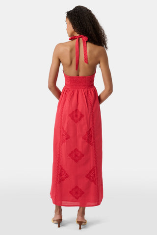 A woman with long curly hair wears the Roller Rabbit Monaco Geo Penelope Dress, a sleeveless, halter-neck, ankle-length red dress with subtle embroidery. She stands forward in open-toed, low-heeled sandals against a plain white background.