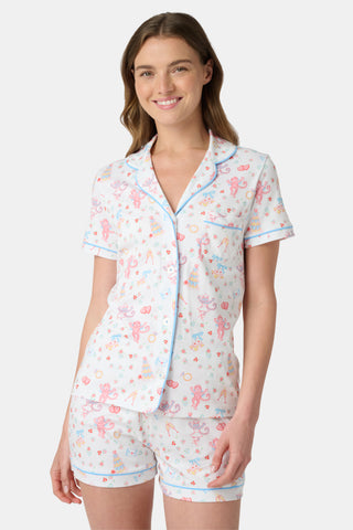 A woman smiles while wearing Roller Rabbit's Monkey Said Yes Polo Pajamas—white short-sleeve top and shorts with colorful, playful prints and blue trim—perfect for bachelorette parties or the newly engaged.