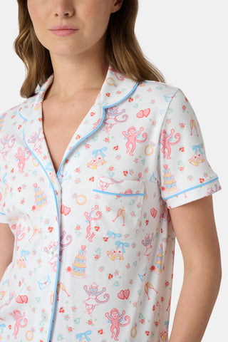 A woman smiles while wearing Roller Rabbit's Monkey Said Yes Polo Pajamas—white short-sleeve top and shorts with colorful, playful prints and blue trim—perfect for bachelorette parties or the newly engaged.