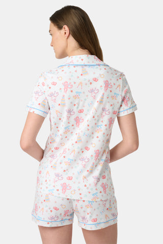 A woman smiles while wearing Roller Rabbit's Monkey Said Yes Polo Pajamas—white short-sleeve top and shorts with colorful, playful prints and blue trim—perfect for bachelorette parties or the newly engaged.