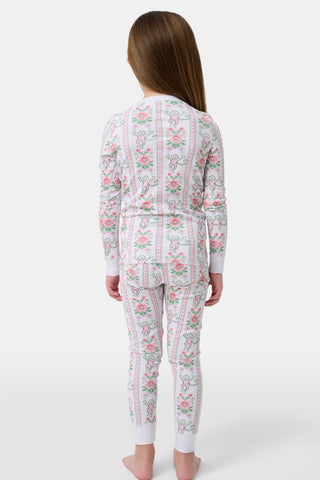 A young girl stands barefoot in Roller Rabbit Kids Monkey Block Stripe Pajamas—matching long-sleeve top and pants with playful monkey block stripes—smiling against a plain light gray background.
