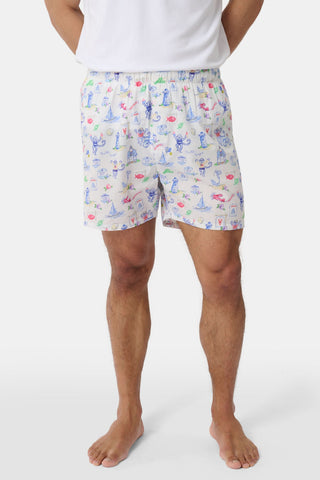 A person wearing a white T-shirt and Roller Rabbit’s Mens Monkey On The Vineyard Boxers, featuring playful and colorful cartoon monkey designs, stands barefoot against a plain white background. The cheerful patterns on the boxers evoke the feel of a summer memento, adding charm to the simple outfit.