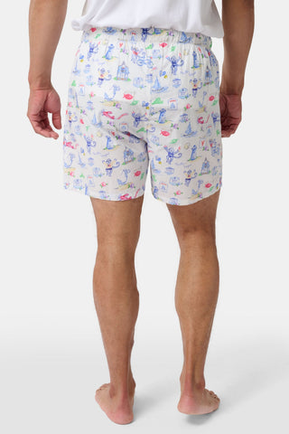 A person wearing a white T-shirt and Roller Rabbit’s Mens Monkey On The Vineyard Boxers, featuring playful and colorful cartoon monkey designs, stands barefoot against a plain white background. The cheerful patterns on the boxers evoke the feel of a summer memento, adding charm to the simple outfit.