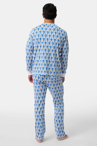A man stands barefoot on a white background, facing away, wearing the Mens Monkey Spencer Pajamas— a matching long-sleeve top and pants set in blue and white with playful cartoon monkeys.