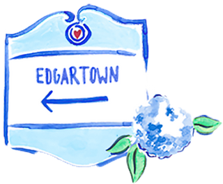 A blue and white illustrated sign featuring Edgartown and a left-pointing arrow, adorned with a blue flower and green leaves.