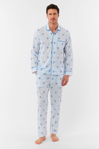 A man stands barefoot wearing the Roller Rabbit Mens Mini Monkey Stripe Loungewear—a cotton pajama set featuring light blue stripes with a small blue floral pattern, long sleeves, and matching pants. He looks at the camera with a slight smile against a plain white background, embodying cozy sleepwear comfort.