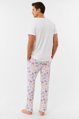 A man stands barefoot against a plain background, wearing the Roller Rabbit Mens Tinned or Twist Milo Set—a Pima cotton T-shirt paired with colorful drawstring waist pants featuring cartoon food patterns.