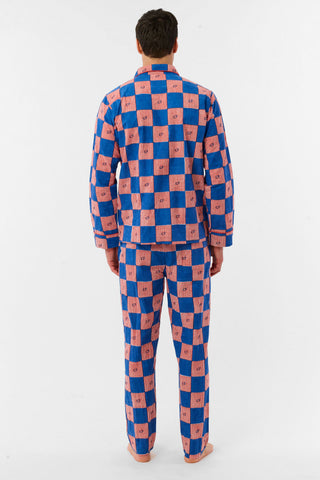 A man with short brown hair and a neutral expression stands barefoot against a white background, wearing the Roller Rabbit Mens Moby Grand Prix Loungewear set in blue and pink checkered cotton with long sleeves and pants.