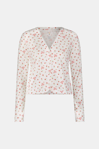 A woman wearing the Roller Rabbit Mini Monkey Blossom Pointelle Allie V-Neck Cardigan—a long-sleeve, white pajama top featuring a small pink floral print and crafted from soft Pima cotton—stands against a plain white background, smiling gently.