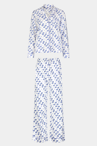 A woman stands barefoot in the Roller Rabbit Moby Long Sleeve Polo Pajamas, featuring a blue geometric-patterned white top and pants. Made from soft pima cotton, the comfy set is shown against a plain white background.