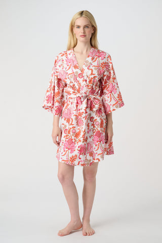 A woman in the Roller Rabbit Amanda Kimono, a pink and white floral cotton robe with wide sleeves and a tie waist, stands against a white background, looking down with a gentle smile.