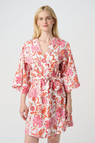 A woman in the Roller Rabbit Amanda Kimono, a pink and white floral cotton robe with wide sleeves and a tie waist, stands against a white background, looking down with a gentle smile.