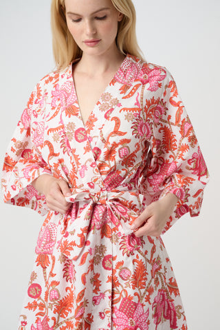 A woman in the Roller Rabbit Amanda Kimono, a pink and white floral cotton robe with wide sleeves and a tie waist, stands against a white background, looking down with a gentle smile.