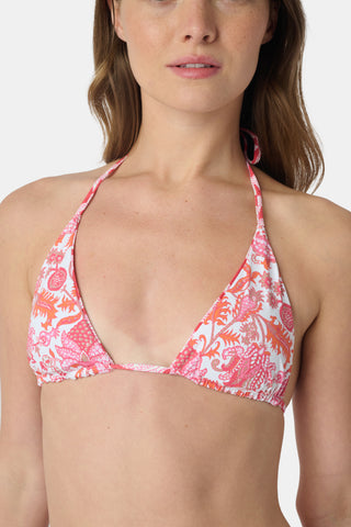 A woman smiles at the beach while holding a straw hat, wearing the Roller Rabbit Amanda/Jemina Serena Bikini Top for stylish sun protection with the ocean and sky behind her.