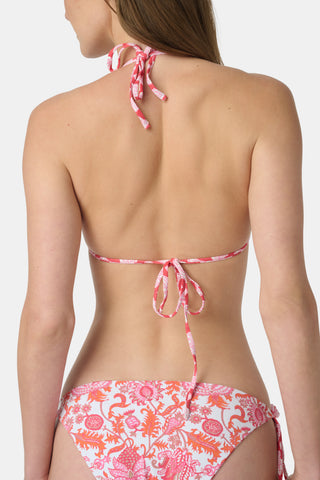 A woman smiles at the beach while holding a straw hat, wearing the Roller Rabbit Amanda/Jemina Serena Bikini Top for stylish sun protection with the ocean and sky behind her.