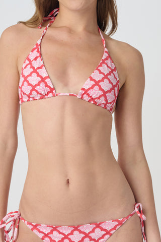 A woman smiles at the beach while holding a straw hat, wearing the Roller Rabbit Amanda/Jemina Serena Bikini Top for stylish sun protection with the ocean and sky behind her.