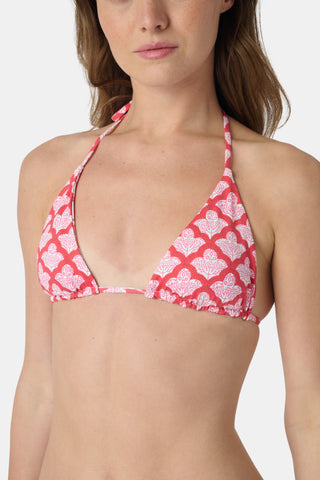 A woman smiles at the beach while holding a straw hat, wearing the Roller Rabbit Amanda/Jemina Serena Bikini Top for stylish sun protection with the ocean and sky behind her.