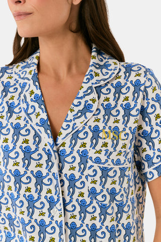 A woman with long blonde hair wears the Roller Rabbit Monkey Polo Pajamas, a matching pima cotton set with a blue and white floral and bird pattern, standing against a plain white background.