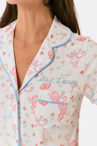 A woman smiles while wearing Roller Rabbit’s Monkey Said Yes Polo Pajamas—a short-sleeved, button-up top and matching shorts with a colorful, playful print featuring whimsical illustrations.