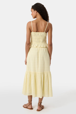 A person wears the Roller Rabbit Petal Eyelet Goldie Skirt, a butter yellow midi with eyelet details, ruffled hem, and gathered top, paired with strappy brown sandals. Their hands rest relaxed by their sides.