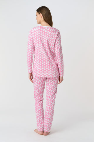 A woman stands barefoot against a plain background, wearing Roller Rabbit's Hathi Pajamas—a matching pink and white set with long sleeves and pants. She faces forward, smiling softly.
