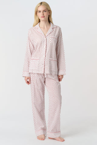 A person with long blonde hair stands barefoot, wearing Roller Rabbit's Hearts Loungewear pajama set—a block-printed cotton ensemble with a light background and small red and blue dots, featuring a buttoned collared top with front pockets.