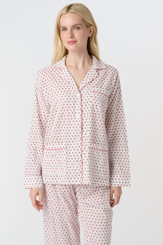 A person with long blonde hair stands barefoot, wearing Roller Rabbit's Hearts Loungewear pajama set—a block-printed cotton ensemble with a light background and small red and blue dots, featuring a buttoned collared top with front pockets.