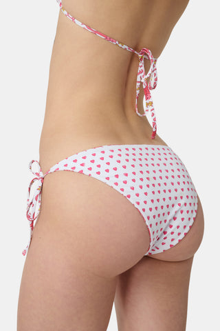 Someone wears the Roller Rabbit Monkey/Hearts Serena Bikini Bottom, a white reversible bikini bottom with pink and red animal and floral patterns, side ties, and UPF 50+ protection. Upper body and hips visible; plain white background.