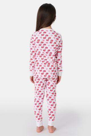 A young girl with curly hair stands barefoot, wearing Kids Moby Pajamas featuring a pink and red pattern. She faces forward with a relaxed expression against a plain white background.