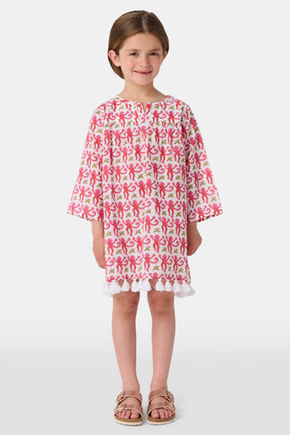 A young girl with brown hair smiles and stands against a white background wearing the Roller Rabbit Kids Monkey Serafina Tunic, a white cotton voile nightgown featuring a playful monkey print and ruffled hem.