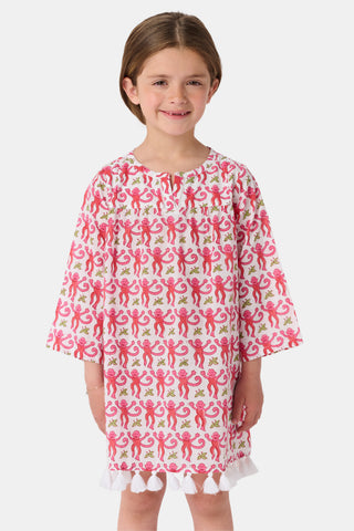 A young girl with brown hair smiles and stands against a white background wearing the Roller Rabbit Kids Monkey Serafina Tunic, a white cotton voile nightgown featuring a playful monkey print and ruffled hem.