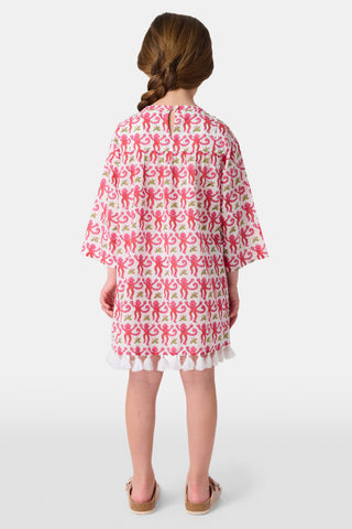 A young girl with brown hair smiles and stands against a white background wearing the Roller Rabbit Kids Monkey Serafina Tunic, a white cotton voile nightgown featuring a playful monkey print and ruffled hem.