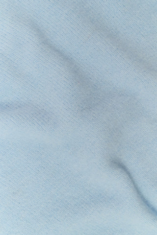 A girl wearing a light blue Kids Coco Sweater in merino-cashmere over a blue patterned dress.