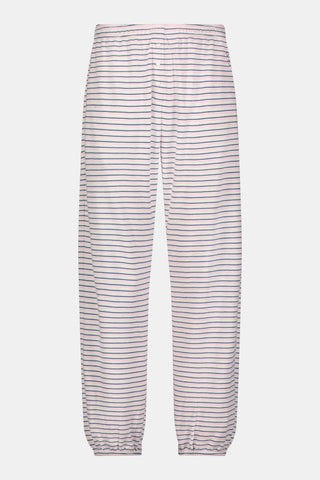 A person stands barefoot on a white background wearing the Roller Rabbit Striped Eva Pant—loose, light-colored pima cotton pajama pants featuring thin blue and red horizontal stripes. Their top is lifted slightly, revealing the elastic waistband.