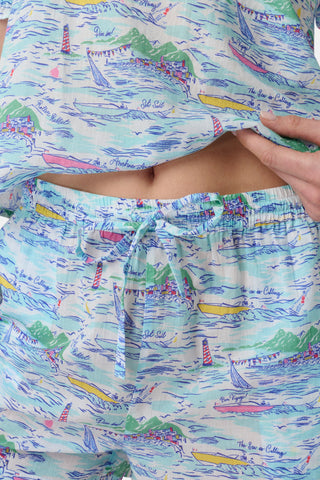 A woman stands facing forward wearing the Roller Rabbit Regatta Preston Set, a light blue and pastel-patterned women's two-piece with short sleeves and matching shorts, paired with white sandals against a plain white background.