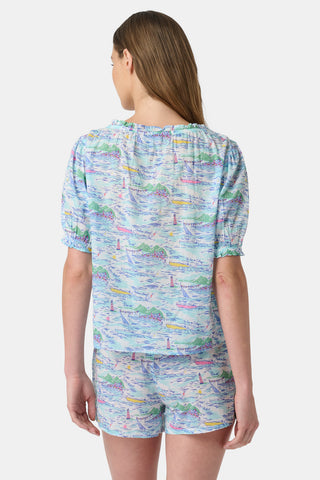 A woman stands facing forward wearing the Roller Rabbit Regatta Preston Set, a light blue and pastel-patterned women's two-piece with short sleeves and matching shorts, paired with white sandals against a plain white background.