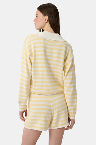 A person wears Roller Rabbit’s Striped Brie Short—a knit yellow and white horizontal striped short with a white drawstring at the elastic waistband and hands tucked in the front pockets.