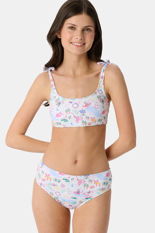 A girl wears the Roller Rabbit Kids Camp RR Cora Bikini, featuring a colorful pattern, adjustable tie straps, and high-waisted bottoms. She smiles against a white background, highlighting the comfort and UV protection of this swimwear.