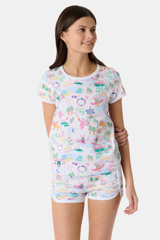 A young girl with long brown hair wears the Roller Rabbit Kids Camp RR Playa Play Set, a 100 Pima Cotton two-piece featuring colorful prints of unicorns, tents, deer, and trees. She faces forward against a plain light background.