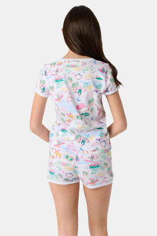 A young girl with long brown hair wears the Roller Rabbit Kids Camp RR Playa Play Set, a 100 Pima Cotton two-piece featuring colorful prints of unicorns, tents, deer, and trees. She faces forward against a plain light background.