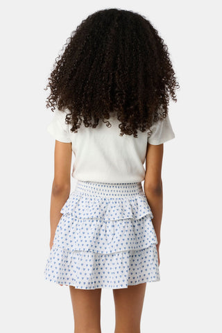 A child wears a white short-sleeved top and the Roller Rabbit Kids Hearts Sami Skirt, featuring three ruffled layers and playful blue heart patterns. The background is plain white.