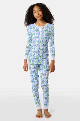 A barefoot child with curly hair wears Kids Leo The Lion Pajamas—a matching long-sleeve Pima cotton set in blue and green with a cartoon lion print—posed against a plain white background.