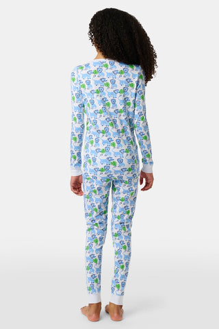A child with curly hair stands barefoot, facing away, wearing Kids Leo The Lion Pajamas—a matching long-sleeve set featuring a colorful cartoon animal pattern on a white background.